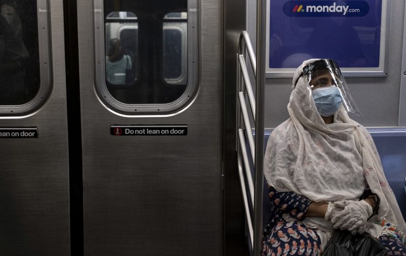 A woman wearing a face mask and shield sits in a subway train during rush hour amid the coronavirus pandemic on July 16, 2020, in New York City. (Photo by Johannes EISELE / AFP)