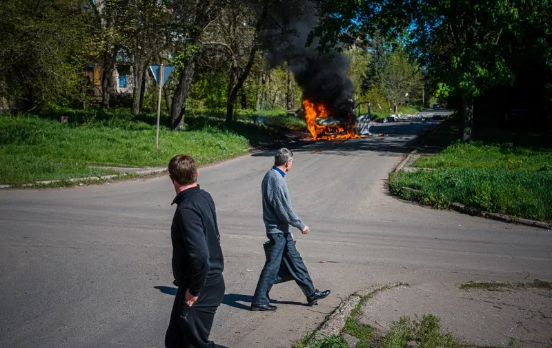 Local residents look at a car burning after a shelling in a street of Kostyantynivka, Donetsk region on May 3, 2023, amid the Russian invasion of Ukraine. (Photo by Dimitar DILKOFF / AFP)