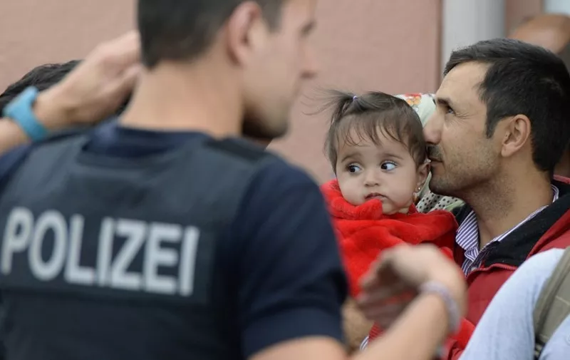 Refugee (R) with child on his arm waits for a special train at the railway station in Freilassing, near the Austrian-German border, southern Germany, on September 15, 2015, after changing from an express train coming from Hungary and Austria. Around 2,000 migrants have crossed into the southern state of Bavaria since Germany announced its policy U-turn on September 13, 2015, federal police said on September 15, albeit at a slower pace than in recent weeks.  AFP PHOTO / CHRISTOF STACHE