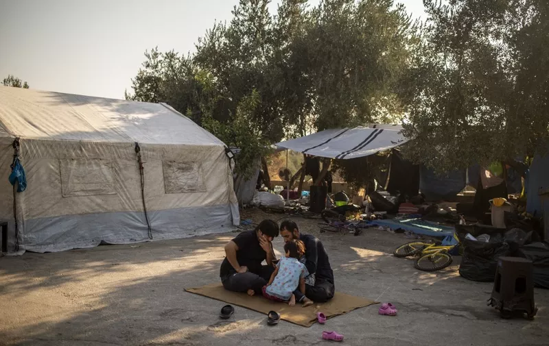 Migrants sit on the ground next to a tent near the burnt Moria refugee camp, on the island of Lesbos on September 13, 2020, a few days after a fire destroyed the camp. - Greece said on September 13 it hoped thousands of asylum seekers left homeless by fires at Europe's largest migrant camp could be rehoused within a week to end a crisis that has seen clashes with police. Asylum-seekers, including the elderly and very young children, have been sleeping rough on Lesbos island since September 9, when some 11,000 fled the overcrowded Moria camp after it was gutted in apparent arson attacks. (Photo by ANGELOS TZORTZINIS / AFP)