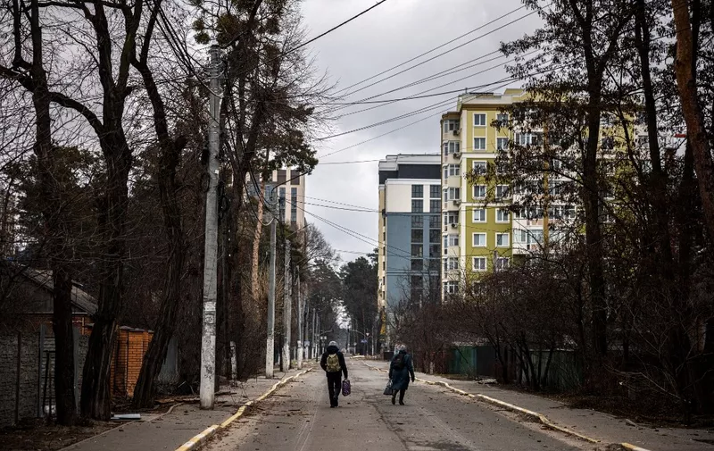 A couple walks down a street as they flee the city of Irpin, northwest of Kyiv, on March 13, 2022. Russian forces advance ever closer to the capital from the north, west and northeast. Russian strikes also destroy an airport in the town of Vasylkiv, south of Kyiv. A US journalist was shot dead and another wounded in Irpin, a frontline northwest suburb of Kyiv, medics and witnesses told AFP. (Photo by Dimitar DILKOFF / AFP)