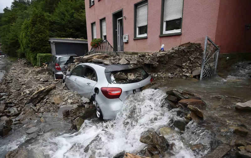 Water runs past a house with a car covered in rubble after heavy rain and floods caused major damage in Hagen, western Germany, on July 15, 2021. - Heavy rains and floods lashing western Europe have killed at least 42 people in Germany and left many more missing, as rising waters led several houses to collapse. (Photo by INA FASSBENDER / AFP)