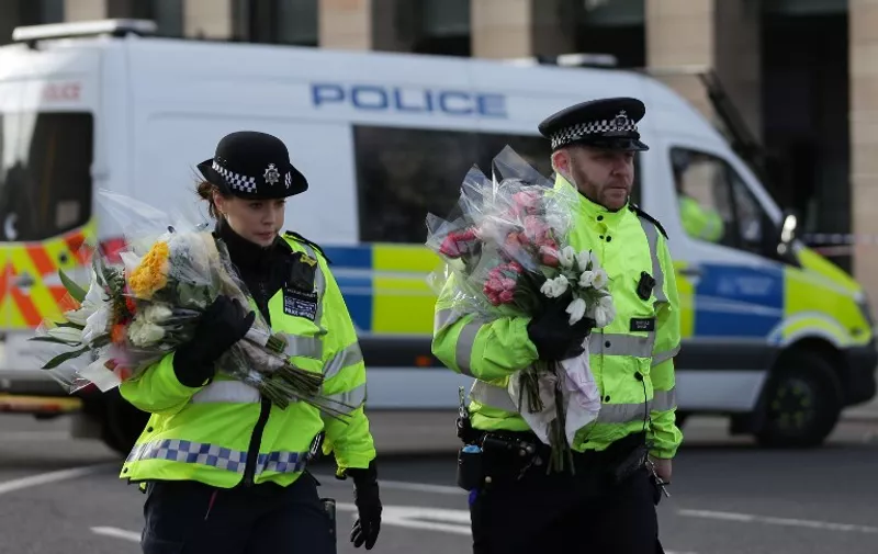 Police officers arrive carrying bunches of flowers to lay in honour of the victims of the March 22 terror attack at the end of Westminster Bridge by the Houses of Parliament in central London on March 23, 2017 after the bridge reopened. 
Britain's parliament reopened on Thursday with a minute's silence in a gesture of defiance a day after an attacker sowed terror in the heart of Westminster, killing three people before being shot dead. Sombre-looking lawmakers in a packed House of Commons chamber bowed their heads and police officers also marked the silence standing outside the headquarters of London's Metropolitan Police nearby.
 / AFP PHOTO / DANIEL LEAL-OLIVAS