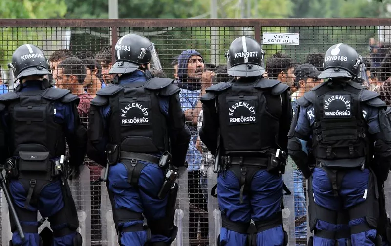 Hungarian riot police officers stand in front of a metal fence that surrounds hundreds of refugees after riots broke out at the local refugee camp in Debrecen town, about 220 km east from Budapest, Hungary, on June 29, 2015. Hungarian police fired tear gas to contain the riot at the overcrowded refugee camp in the eastern city of Debrecen after fighting broke out between asylum seekers over a religious dispute. The disturbance began after one migrant ran off with another's copy of the Koran and trampled on it, said a statement on the Hungarian police website.  AFP PHOTO / STEVEN DEBORA