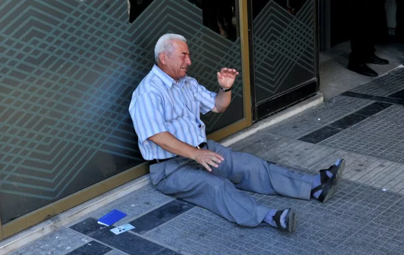 A distressed pensioner sits on the ground outside a national bank branch, as banks opened only for pensioners to allow them to withdraw their pensions, with a limit of 120 euros, in Thessaloniki, on July 3, 2015. Greece is almost evenly split over a crucial weekend referendum that could decide its financial fate, with a 'Yes' result possibly ahead by a whisker, the latest survey Friday showed. Prime Minister Alexis Tsipras's government is asking Greece's voters to vote 'No' to a technically phrased question asking if they are willing to accept more tough austerity conditions from international creditors in exchange for bailout funds. AFP PHOTO /SAKIS MITROLIDIS
