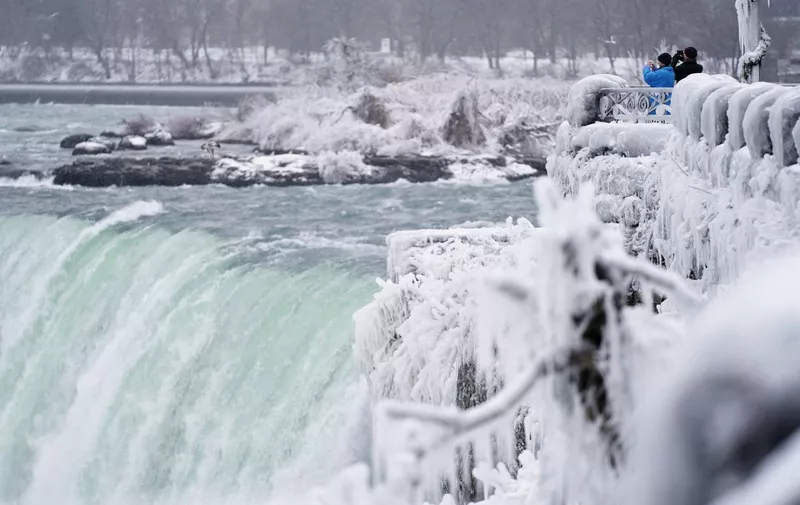 Two men take photographs at the Horseshoe Falls in Niagara Falls, Ontario, on January 27, 2021. (Photo by Geoff Robins / AFP)