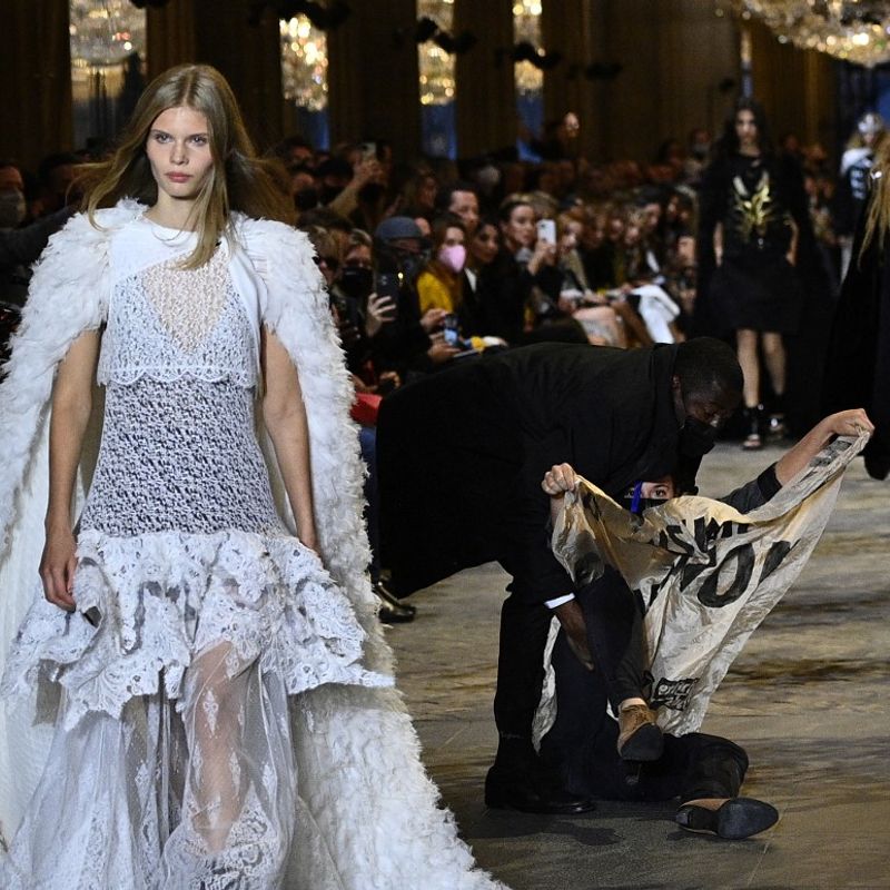 A demonstrator is being evicted by a security member as a model presents a creation by Louis Vuitton during the Women's Spring-Summer 2022 Ready-to-Wear collection fashion show as part of Paris Fashion Week at the Louvre in Paris, on October 5, 2021. - Extinction Rebellion activists burst into the Louis Vuitton fashion show at the Louvre to denounce the impact of the fashion industry on climate change, on the last day of Paris Fashion Week. (Photo by Christophe ARCHAMBAULT / AFP)