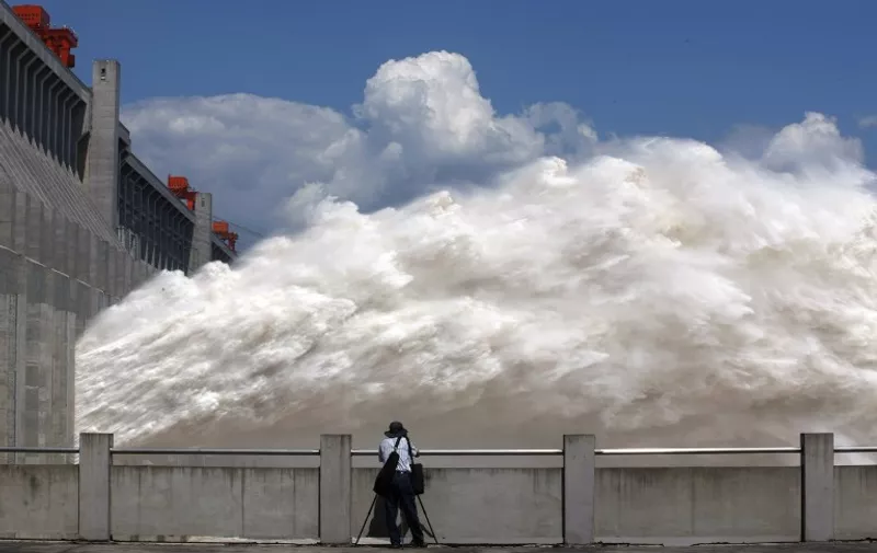 This picture taken on September 3, 2014 shows a man taking pictures of floodwater released from the Three Gorges Dam, a gigantic hydropower project on the Yangtze river, in Yichang, central China's Hubei province, after heavy downpours in the upper reaches of the dam caused the highest flood peak of the year. Eleven people died and 27 others are missing after torrential rains battered southwest China's Chongqing, a municipality in the upper reaches of the Three Gorges Dam, causing thousands of houses to collapse, state media said.    CHINA OUT     AFP PHOTO