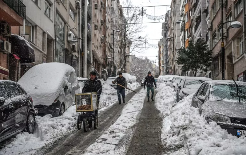 A street vendors walk on a street after a snowfall in Istanbul on January 10, 2017. 
Heavy snowstorms also reached Turkey over the weekend, paralysing its biggest city Istanbul where almost 65 centimetres (25 inches) of snow fell, forcing hundreds of flights to be cancelled on January 7. / AFP PHOTO / OZAN KOSE