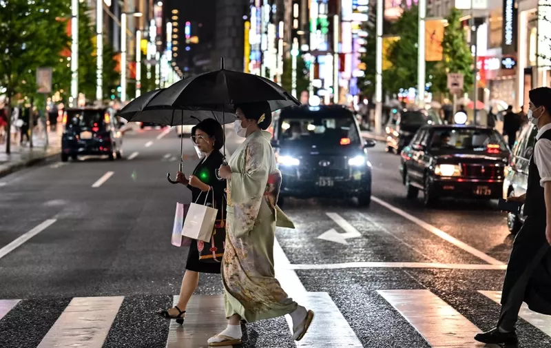 Pedestrians cross a street during a rainy evening in Tokyo on October 7, 2020. (Photo by CHARLY TRIBALLEAU / AFP)
