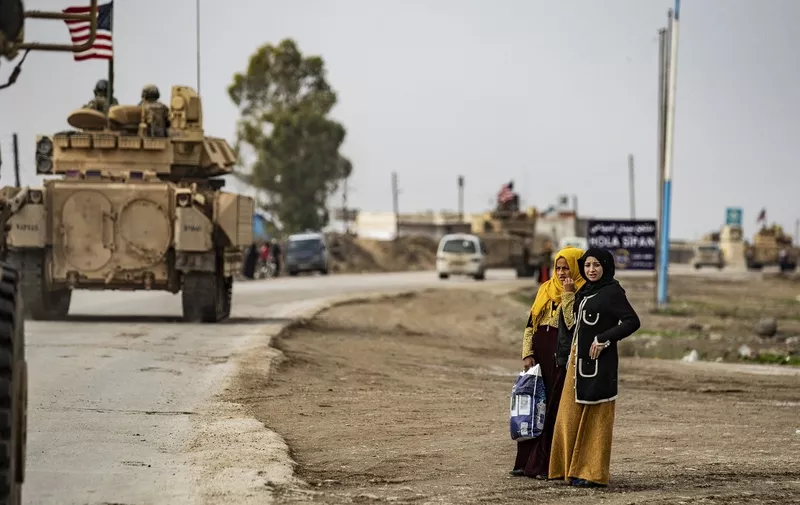 Women watch as US troops patrol in their military vehicles on the roads of the Syrian town of al-Jawadiyah and meet the inhabitants, in the northeastern Hasakeh province, near the border with Turkey, on December 17, 2020. (Photo by Delil SOULEIMAN / AFP)