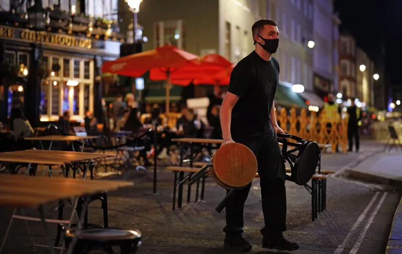 A member of staff takes away stools from outside tables in Soho, in central London on September 24, 2020, on the first day of the new earlier closing times for pubs and bars in England and Wales, introduced to combat the spread of the coronavirus. - Britain has tightened restrictions to stem a surge of coronavirus cases, ordering pubs to close early and advising people to go back to working from home to prevent a second national lockdown. (Photo by Tolga Akmen / AFP)