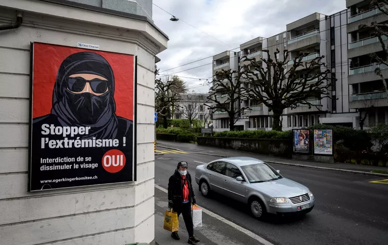 A man wearing a face mask walks on February 4, 2021 in Lausanne past an electoral poster in favor of a "burqa ban" initiative reading in French: "Stop extremism!" ahead of a nationwide vote by Swiss citizen on whether they want to ban face coverings in public spaces or not. - The vote will take place on on March 7, 2021, as part of the country's famous direct democratic system. A clear majority of Swiss voters favour introducing a nationwide prohibition against wearing face-covering garments in public spaces, known as a "burqa ban", a poll showed last month. (Photo by Fabrice COFFRINI / AFP)