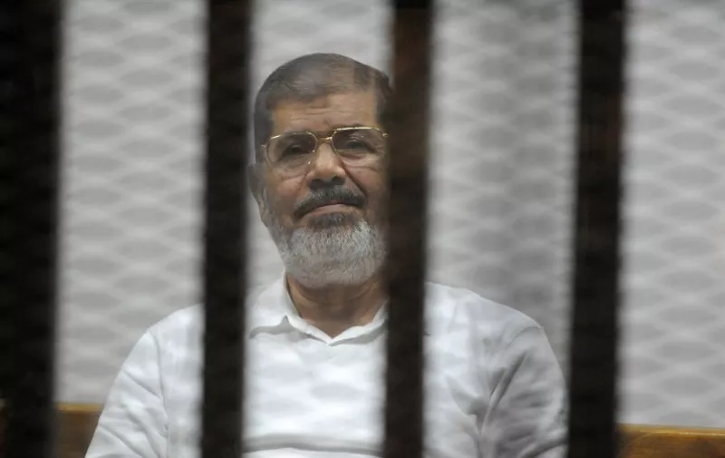 Egypt's deposed Islamist president Mohamed Morsi sists behind the defendants cage during a trial at the police academy court in Cairo on November 5, 2014. Morsi is on trial in several cases and faces a death sentence if convicted of espionage and terrorism related charges. AFP PHOTO / STR