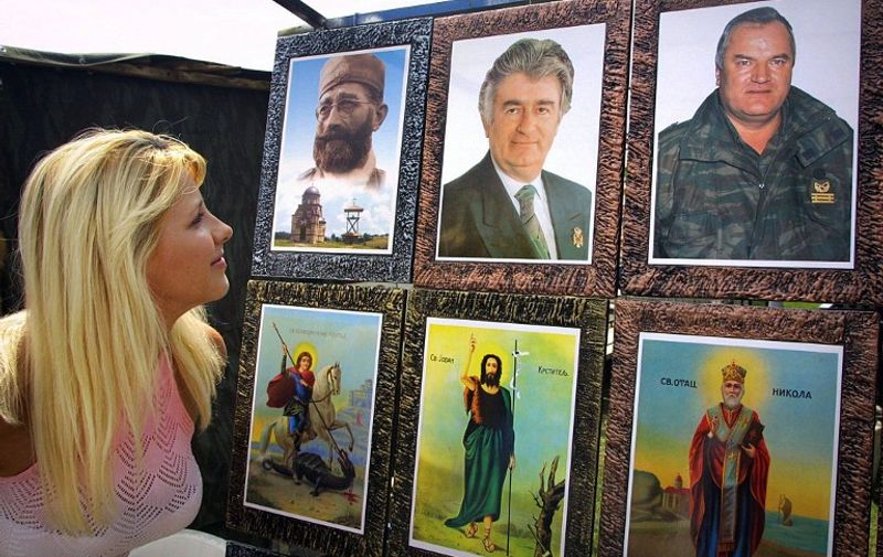 A woman watches pictures of Bosnian Serb wartime leader Radovan Karadzic (upper row, center) and his former army chief Ratko Mladic (upper row, right) - two top fugitives who have been on the run for a decade since they were charged with genocide by the UN war crimes tribunal at The Hague, and Draza Mihailovic, (upper row, left), former leader of Chetniks - Serb royalists who fought both the Nazis and the communist Partisans in World War II, together with pictures of saints important for the Serb Orthodox Church, during the market day in northwestern Bosnian town of Prijedor, 18 June 2005. Bosnian Serb authorities last year admitted to the horrific scale of the 1995 Srebrenica massacre of some 8,000 Muslims by Serb forces, but most ordinary Serbs still deny the truth about the worst single atrocity in Europe since World War II. Some 50,000 people are expected to attend ceremonies to mark the 10th anniversary of the massacre on 11 July.    AFP PHOTO STRINGER