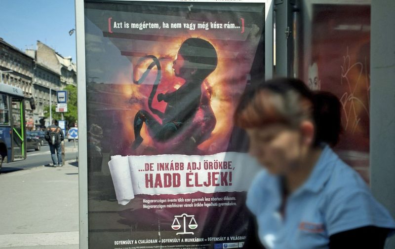 TO GO WITH AFP STORY BY ESZTER BALAZS- A woman waits in front of an anti-abortion poster bearing a picture of a foetus and slogan reading ''I can also understand if you are not yet prepared to receive me, but have me rather adopted and let me live! (down), on May 17, 2011 at a bus-stop in downtown Budapest. Hungary, the current EU president, came under fire from Brussels this week for using European money to fund an anti-abortion campaign.  AFP PHOTO / BEA KALLOS / MTI (Photo by BEA KALLOS / AFP)