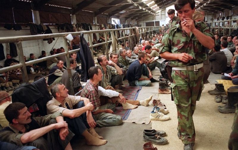 A serbian soldier smoles a cigarette as he guards Bosnian prisoners 14 August 1992 in a farm turned into an internment camp in Manjaca. Some 3.500 Bosnian people are held in the camp as Serbs continue their "ethnic cleansing" operation in Bosnia-Hercegovina.   / AFP PHOTO / ANDRE DURAND