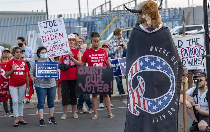 Jake Angeli, 33, aka Yellowstone Wolf, from Phoenix, wrapped in a QAnon flag, addresses supporters of US President Donald Trump as they protest outside the Maricopa County Election Department as counting continues after the US presidential election in Phoenix, Arizona, on November 5, 2020. - President Donald Trump erupted on November 5 in a tirade of unsubstantiated claims that he has been cheated out of winning the US election as vote counting across battleground states showed Democrat Joe Biden steadily closing in on victory. (Photo by OLIVIER  TOURON / AFP)