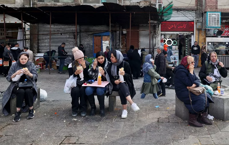 Women eat as they sit in a commercial area in Tehran on February 21, 2023. - Iran's currency plunged to new lows on January 20 amid fresh European Union sanctions, crossing the psychologically important rate of 500,000 rials to a dollar in foreign exchange markets. (Photo by ATTA KENARE / AFP)