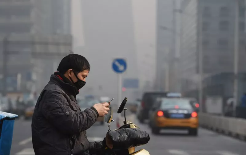 A man checks his smartphone on a polluted day in Beijing on December 14, 2015. Authorities issued a yellow alert for pollution on December 14, the first since a red alert last week.  AFP PHOTO / GREG BAKER / AFP / GREG BAKER