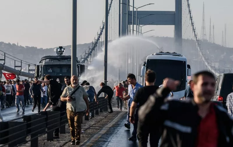 Turkish anti riot police officers use water cannon on people as a police bus carry detained Turkish soldiers after they took over military position on the Bosphorus bridge in Istanbul on July 16, 2016.
The number of dead from a coup attempt in Turkey has risen to 90, the state-run news agency Anadolu reported on July 16, 2016, adding that 1,154 people were wounded. Nearly 200 unarmed soldiers at the Turkish military headquarters have meanwhile surrendered, an official said, adding that special troops were currently securing the complex. / AFP PHOTO / OZAN KOSE