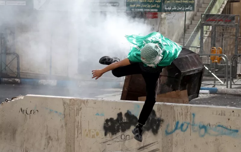 A Palestinian youth jumps as clashes break out with Israeli soldiers during a protest in the occupied West Bank city of Hebron to show solidary with the Palestinians of the Gaza Strip on October 20, 2023, amid ongoing battles between Israel and the Hamas movement. (Photo by MOSAB SHAWER / AFP)