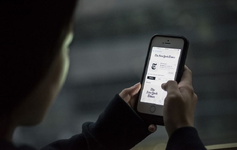 This photo illustration taken on January 5, 2017 in Beijing shows a user posing with an iPhone showing an installed New York Times app on the device. 
Apple has removed the New York Times from its China app store, the tech giant said, after authorities told the company the app breached regulations. / AFP PHOTO / FRED DUFOUR