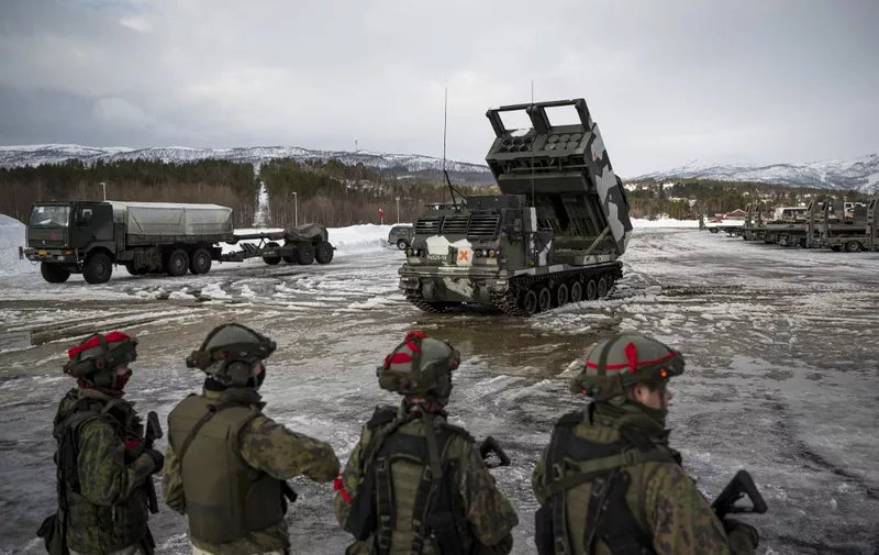 Soldiers from the Finnish Defence Forces stand in front of a M270 Multiple Launch Rocket System, operated by the Finnish Defence Forces, during the international military exercise Cold Response 22, at Setermoen, North of in Norway, on March 22, 2022. - Cold Response is a Norwegian-led winter exercise in which involving 30,000 NATO troops and partner countries and was planned long before Moscow's invasion of Ukraine. (Photo by Jonathan NACKSTRAND / AFP)