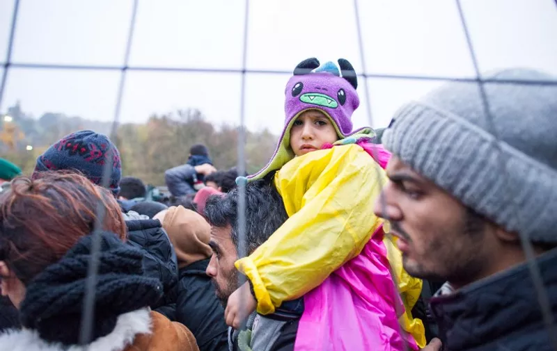 A child looks on as migrants and refugees wait to cross the Slovenian-Austrian border in Sentilj, Slovenia, to Spielfeld, Austria, on October 29, 2015. Austria on October 28  announced plans to build a fence at a major border crossing with fellow EU state Slovenia to "control" the migrant influx, in a blow to the bloc's cherished passport-free Schengen zone. AFP PHOTO / RENE GOMOLJ