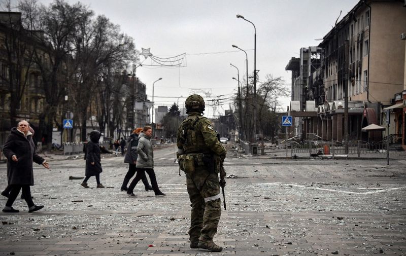 People pass by a Russian soldier in central Mariupol on April 12, 2022, as Russian troops intensify a campaign to take the strategic port city, part of an anticipated massive onslaught across eastern Ukraine, while Russia's President makes a defiant case for the war on Russia's neighbour. - *EDITOR'S NOTE: This picture was taken during a trip organized by the Russian military.* (Photo by Alexander NEMENOV / AFP)