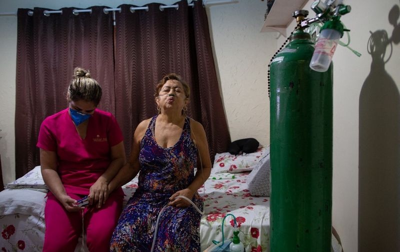 Dilza Maria Pereira Rodrigues (R), 71,  is seen during a physiotherapy session as she recuperates at home after spending 15 days at hospital with COVID-19. (Photo by Michael DANTAS / AFP)