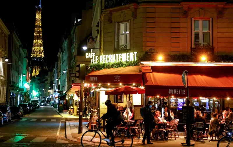 People sit at a cafe terrace as the Eiffel Tower is seen in the background in Paris on October 26, 2020, prior to a nighttime curfew imposed as part of measures aimed at curbing the spread of the Covid-19 pandemic, caused by the novel coronavirus. - A nighttime curfew of 9pm to 6pm came into effect on October 17 for Paris and several other cities in France where coronavirus cases are soaring, and was extended to a toal of 54 departments as of October 23, affecting some 46 million people. A distance of 1 metre between seatings of different tables and a maximum of six people per group is also in place. (Photo by Ludovic MARIN / AFP)