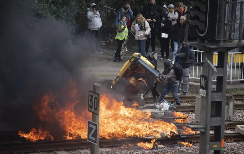 Protesters push a garbage bin into a flaming barricade across railway tracks at a train station during a demonstration after the government pushed a pensions reform through parliament without a vote, using the article 49.3 of the constitution, in Lorient, in Brittany, western France, on March 28, 2023. - France faces another day of strikes and protests nearly two weeks after the president bypassed parliament to pass a pensions overhaul that is sparking turmoil in the country, with unions vowing no let-up in mass protests to get the government to back down. The day of action is the tenth such mobilisation since protests started in mid-January against the law, which includes raising the retirement age from 62 to 64. (Photo by FRED TANNEAU / AFP)