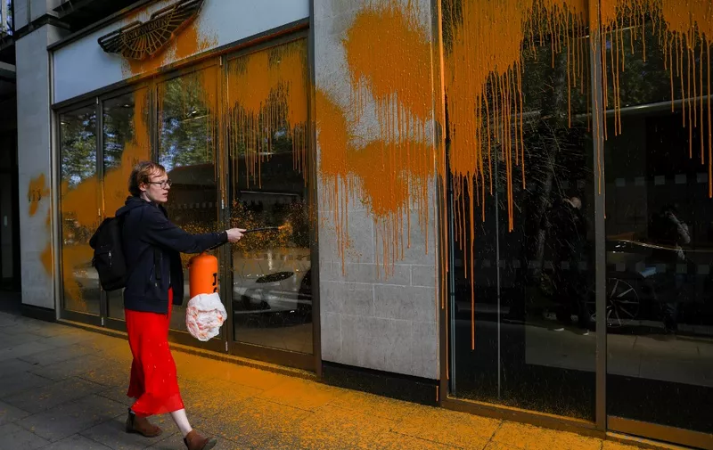 A member of the environmental activist group Just Stop Oil sprays orange paint on the window shop of the Aston Martin car show room, in central London, on October 16, 2022 as part of a series of actions. - Just Stop Oil, which wants an end to new fossil fuel licensing and production, are involved in a month-long series of protests in central London. (Photo by ISABEL INFANTES / AFP)