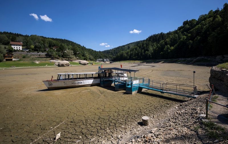 A picture taken on August 4, 2022 in Les Brenets shows the dry bed of Brenets Lake (Lac des Brenets), part of the Doubs River, a natural border between eastern France and western Switzerland, as much of Europe bakes in a third heatwave since June. - The river has dried up due to a combination of factors, including geological faults that drain the river, decreased rainfall and heatwaves. (Photo by Fabrice COFFRINI / AFP)