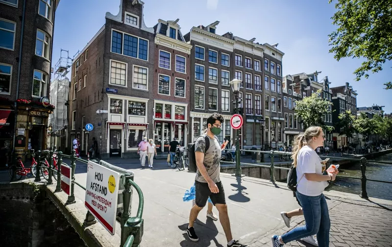 People, wearing a face mask, walk on a bridge of the Red Light district, in Amsterdam on August 5, 2020, as from today, wearing a face mask is mandatory in five usually crowded places in the city of Amsterdam. - France and the Netherlands are gearing up for stricter mask-wearing rules to fight the coronavirus as the global death toll from the pandemic neared 700,000. (Photo by Remko DE WAAL / ANP / AFP) / Netherlands OUT