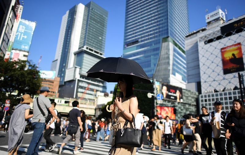 A woman protects herself from the sun with an umbrella during a heatwave as she crosses the street in Tokyo's Shibuya district on August 4, 2019. (Photo by Charly TRIBALLEAU / AFP)