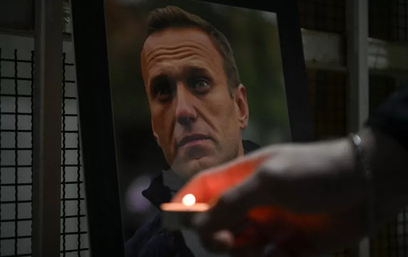 A person lights a candle by a portrait of late Russian opposition leader Alexei Navalny, who died in a Russian Arctic prison, placed at the entrance of the Chancery of the Embassy of the Russian Federation in Pristina on February 20, 2024. (Photo by Armend NIMANI / AFP)