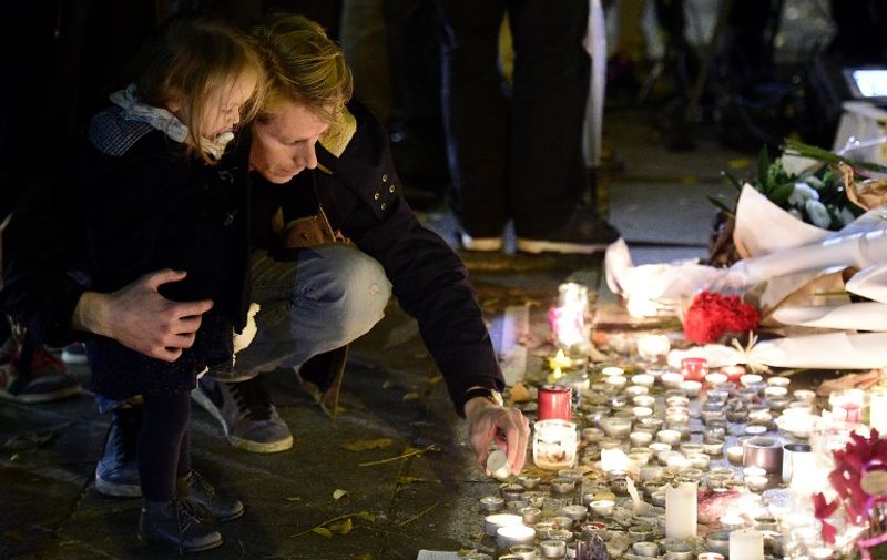 A man puts a candle at a makeshift flowers and candles memorial near the Bataclan concert hall on November 14, 2015 in Paris, a day after a series of coordinated attacks in and around Paris. Islamic State jihadists claimed a series of coordinated attacks by gunmen and suicide bombers in Paris that killed at least 129 people in scenes of carnage at a concert hall, restaurants and the national stadium. AFP PHOTO / FRANCK FIFE