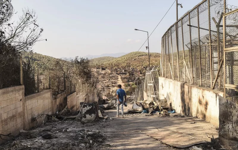 A migrant walks in the burnt camp of Moria on the island of Lesbos, a few days after a fire destroyed the Moria refugee camp, on September 13, 2020. - Tension was simmering on September 12 on Greece's Lesbos island as thousands of asylum seekers remained homeless four days after Europe's largest migrant camp was destroyed by fire. Round-the-clock efforts to find temporary shelter for over 11,000 people including thousands of children were still inadequate, rights groups said as local authorities continued to oppose camp reconstruction plans. (Photo by ANGELOS TZORTZINIS / AFP)