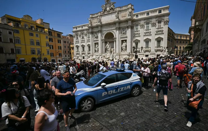 A general view taken on May 21, 2023 shows a polce car parked by the Fontana di Trevi fountain in downtown Rome as tourists walk past, after environmental activists of Last Generation (Ultima Generazione) poured black liquid made out of vegetable-based carbon into the water as part of a campaign to raise awareness about climate change. (Photo by Filippo MONTEFORTE / AFP)