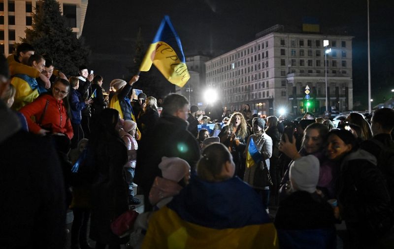 People hold a Ukranian flag as they gather in Maidan square to celebrate the liberation of Kherson, in Kyiv on November 11, 2022, amid the Russian invasion of Ukraine. - Ukraine's President Volodymyr Zelensky said on November 11 that Kherson was "ours" after Russia announced the completion of its withdrawal from the regional capital, the only one Moscow captured in nearly nine months of fighting. (Photo by Genya SAVILOV / AFP)