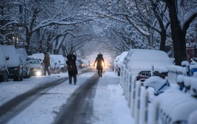 People walk through snow along a street in Brooklyn borough of New York during the first snow storm of the season on January 7, 2022. (Photo by Ed JONES / AFP)