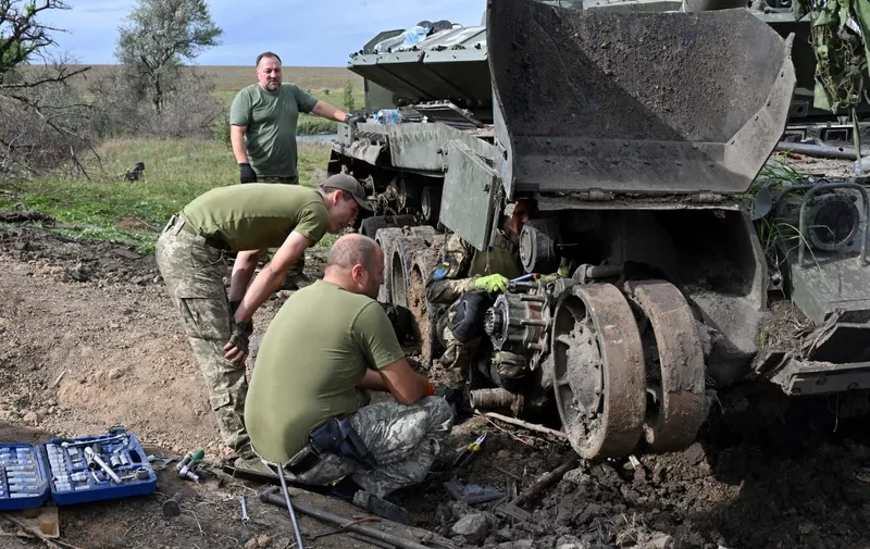 Ukrainian servicemen work on a tank on September 20, 2022, abandoned by Russian troops during their retreat in the north of the Kharkiv region. (Photo by SERGEY BOBOK / AFP)