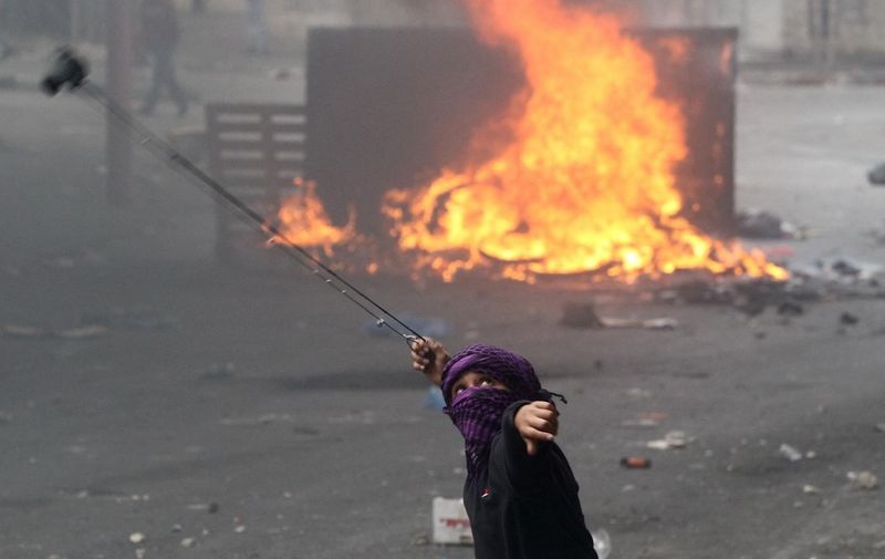 A Palestinian youth uses a slingshot to throw a stone towards Israeli security forces during clashes near an Israeli checkpoint in the West Bank town of Hebron on October 6, 2015. Palestinian president Mahmud Abbas said he wanted to avoid a violent escalation with Israel, his most direct comments since unrest has spread and provoked fears of a new uprising. AFP PHOTO / HAZEM BADER (Photo by HAZEM BADER / AFP)