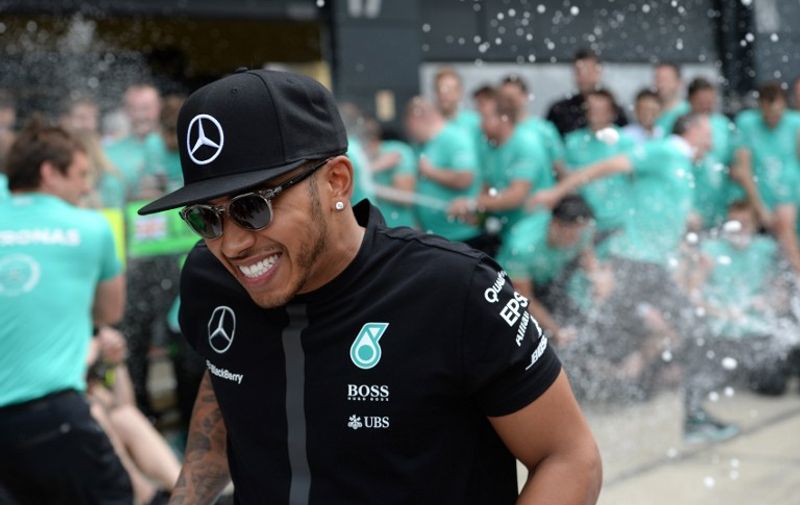 Mercedes AMG Petronas F1 Team's British driver Lewis Hamilton runs as champagne is uncorked after a team photo in the pits after the British Formula One Grand Prix at the Silverstone circuit in Silverstone on July 5, 2015.  
