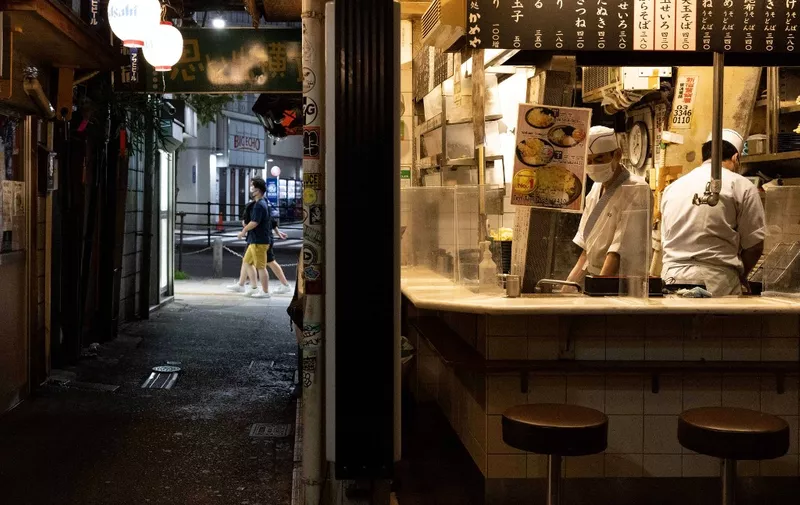 Staff work at a tempura shop in a quiet alleyway in the Shinjuku district of Tokyo on July 17, 2021, after the city recorded its highest number of Covid-19 coronavirus cases since January, with less than a week before the opening ceremony for the 2020 Olympic Games. (Photo by Yuki IWAMURA / AFP)