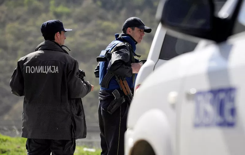 Police officers guard a check point as a vehicle of the   Organization for Security and Co-operation in Europe (SCE) passes, on the road to the village of Goshince, from where police officers were taken hostage overnight, north of the capital Skopje on April 21, 2015. About 40 armed men wearing uniforms of a disbanded ethnic Albanian guerrilla army from Kosovo took several police officers hostage in northern Macedonia overnight, Macedonian police said on on April 21. AFP  PHOTO / ROBERT ATANASOVSKI (Photo by ROBERT ATANASOVSKI / AFP)