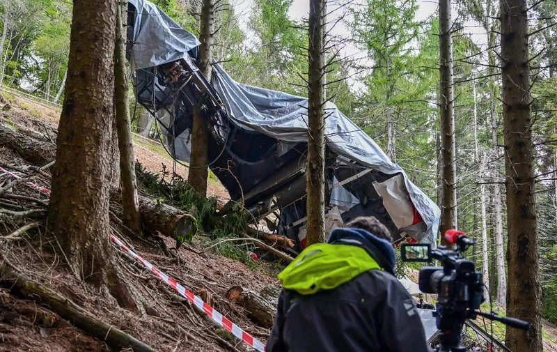 A view shows a journalist working by the cabin's wreckage covered with a tarpaulin on May 26, 2021 on the slopes of the Mottarone peak above Stresa, Piedmont, three days after a cable car crash that killed 14. - Investigators probed the causes of a terrifying cable car crash in the Italian mountains that left 14 people dead, including five Israelis, and a young child fighting for life. (Photo by MIGUEL MEDINA / AFP)