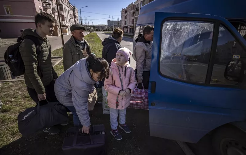 People wait for a bus as a children looks at the sky, a day after a rocket attack at a train station, in Kramatorsk, on April 9, 2022. - At least 52 people were killed, including five children, following a rocket attack on April 8 on a train station in the eastern Ukrainian city of Kramatorsk that is being used for civilian evacuations, according to Donetsk region governor. (Photo by FADEL SENNA / AFP)